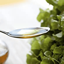 Un dosaggio che aiuta Primo piano di un cucchiaio con olio su sfondo bianco con erbe