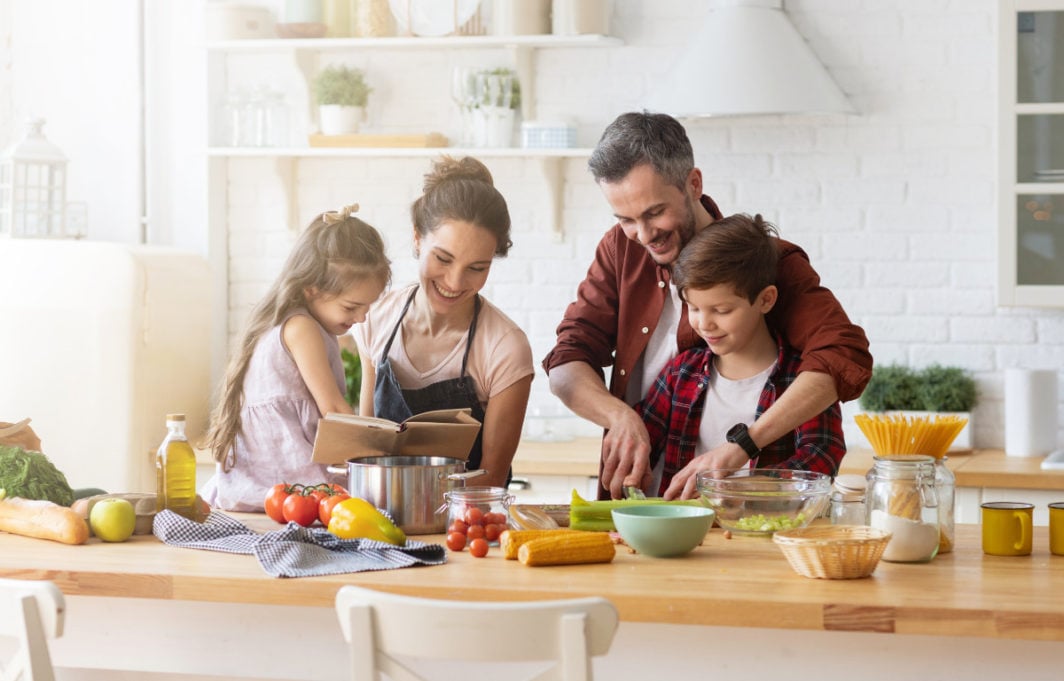 Madre, padre, figlia e figlio cucinando insieme, tutti sorridendo