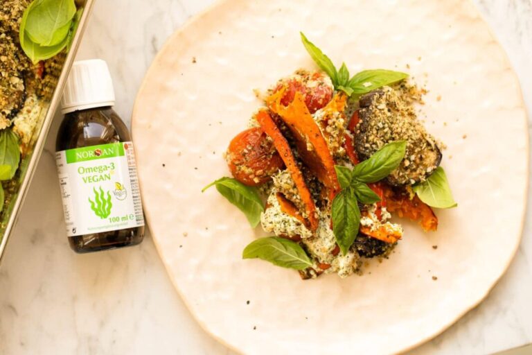 Vista dall'alto, lo stufato di zucca con pomodori, basilico e peperoni. Accanto c'è una bottiglia di NORSA Omega-3 Vegano.